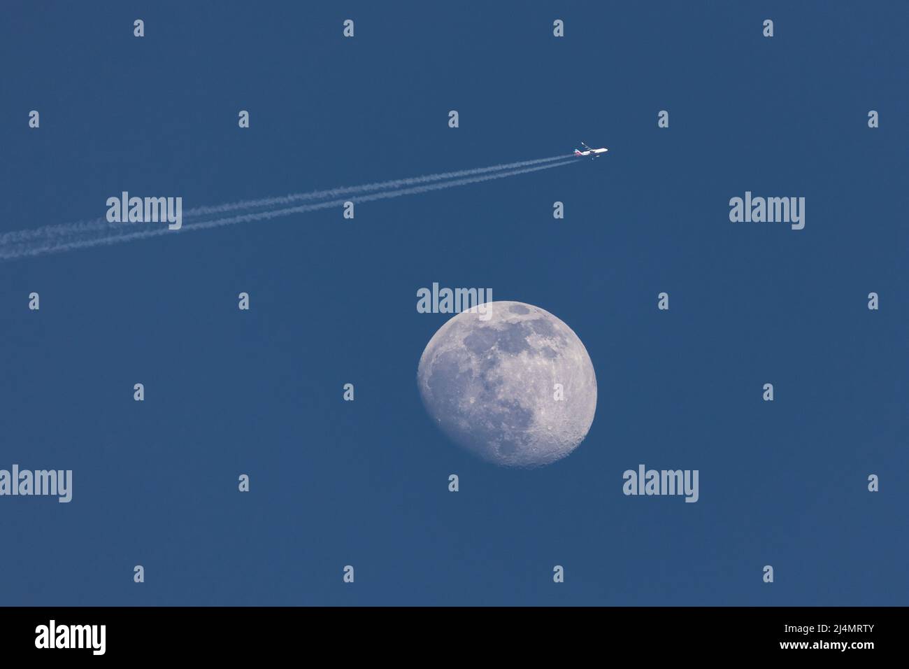 Primo piano della luna ceretta e un aeroplano che passa vicino, lasciando un contrail - cattura di prima sera contro il cielo blu scuro. Stoccarda, Germania Apr Foto Stock