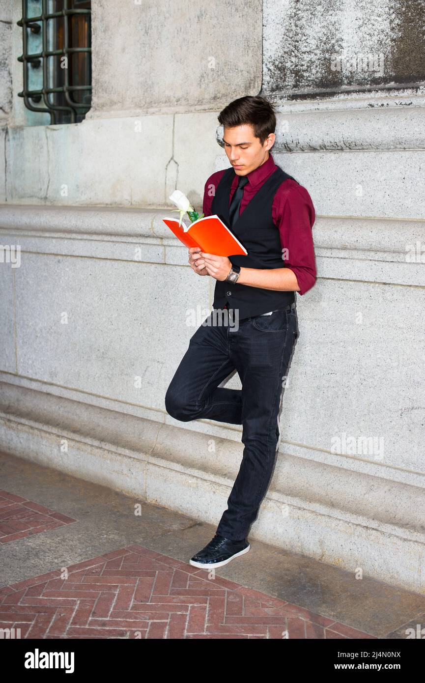 Vestendo in una camicia rossa, un gilet nero, jeans neri e una cravatta nera,  un ragazzo bello giovane sta leggendo un libro rosso con una rosa bianca  Foto stock - Alamy