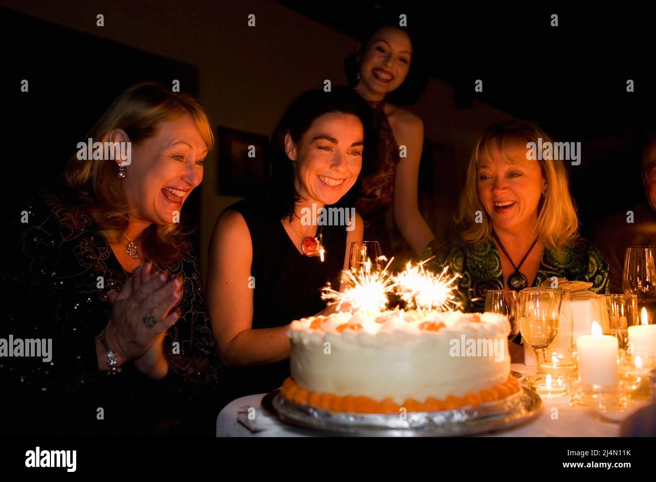 Quattro donne che guardano scintille sulla torta di compleanno a festa Foto Stock