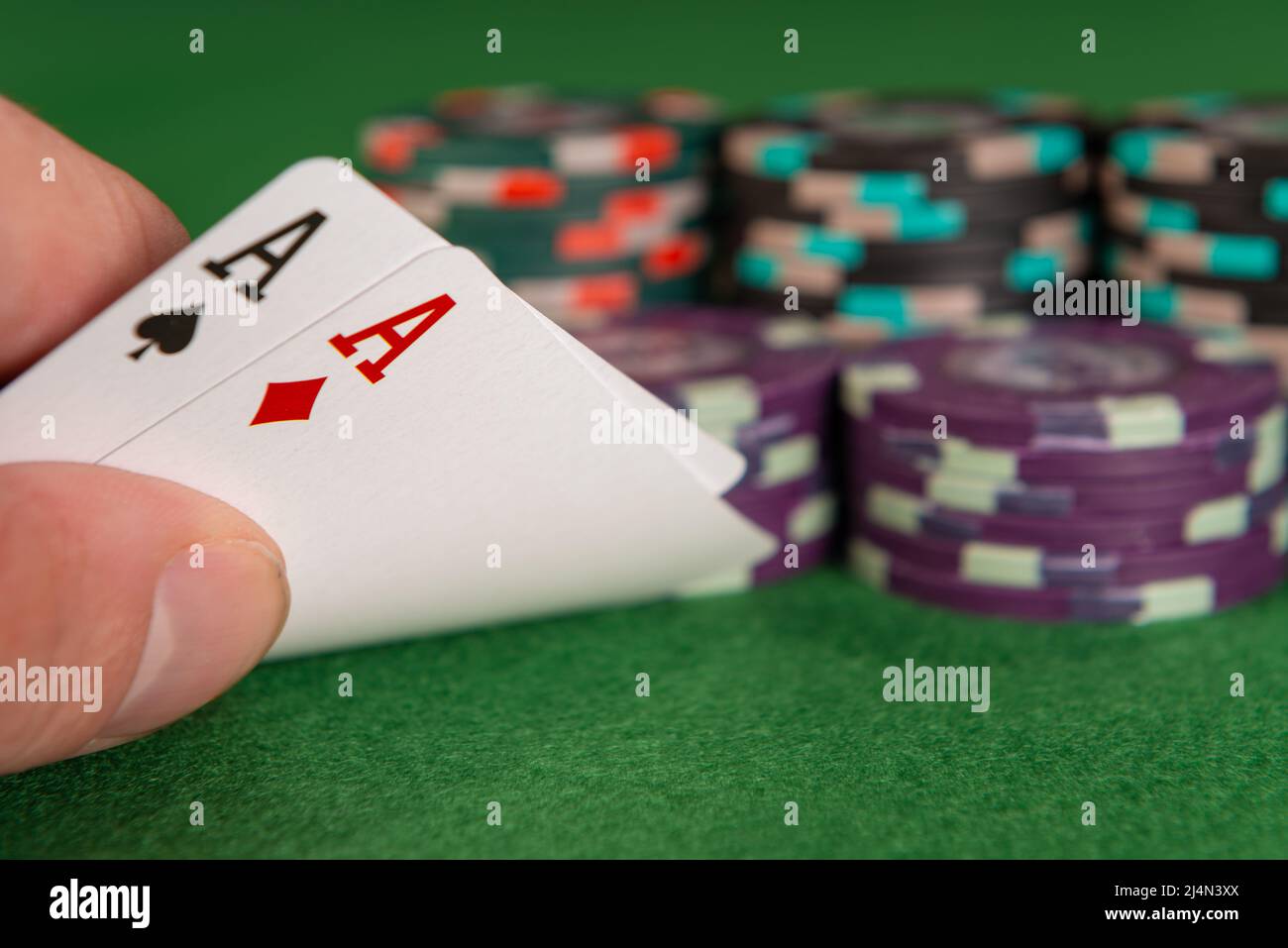 Una mano caucasica solleva l'angolo di due carte da gioco, rivelando che entrambe sono assi. Sullo sfondo ci sono diverse pile di chip. Foto Stock