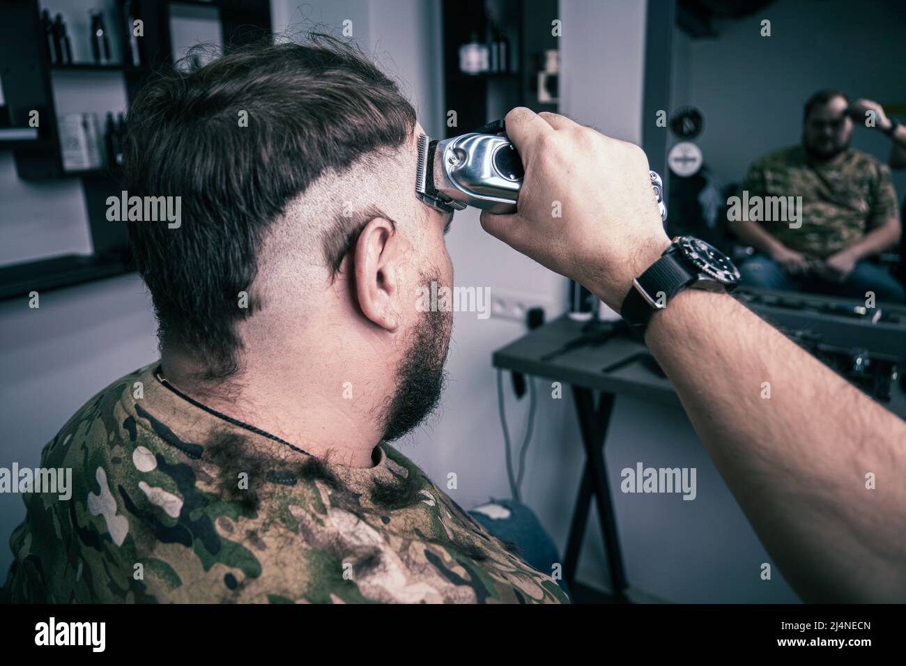 Un giovane uomo in uniforme militare rasa la testa calva per il servizio militare. Un ragazzo con una barba ottiene un taglio di capelli ad un negozio di barbiere. Foto Stock