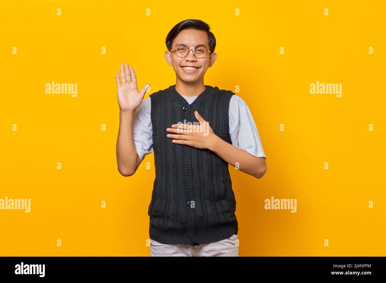 Giovane asiatico sorridente e saluto isolato su sfondo giallo Foto Stock