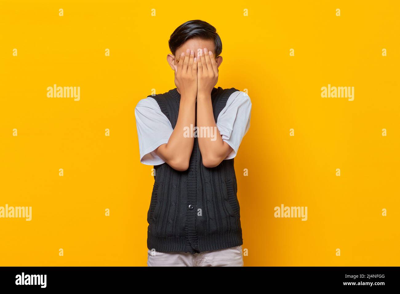 Ritratto di bel giovane uomo che ricopre il volto con palme su sfondo giallo Foto Stock