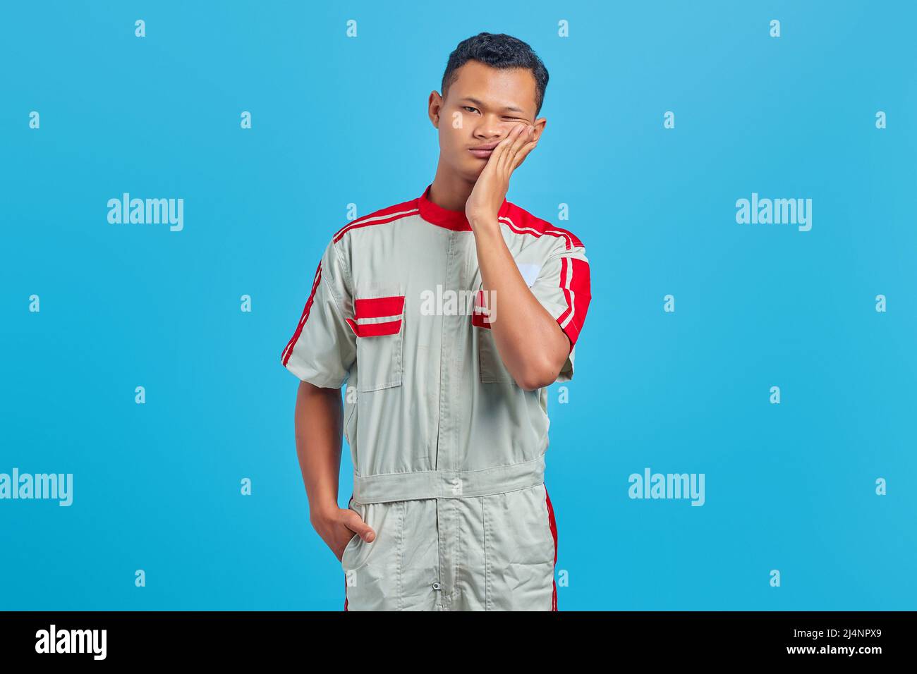 Ritratto di giovane meccanico asiatico che tocca la bocca con espressione dolorosa su sfondo blu Foto Stock