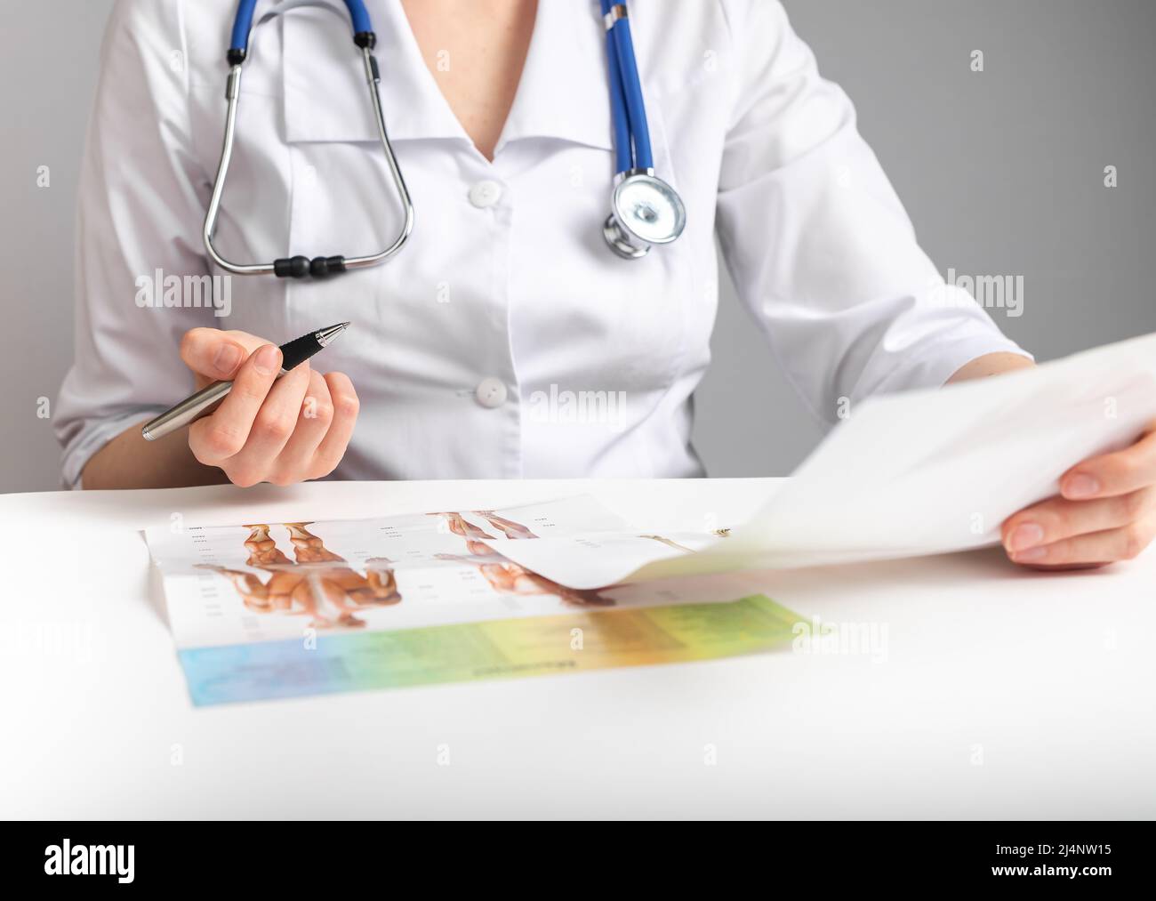 Dottore che tiene carte e studia anatomia. Educazione medica e concetto di conduzione della ricerca. Donna in camice da laboratorio con stetoscopio seduto a tavola e documenti di analisi. Foto di alta qualità Foto Stock