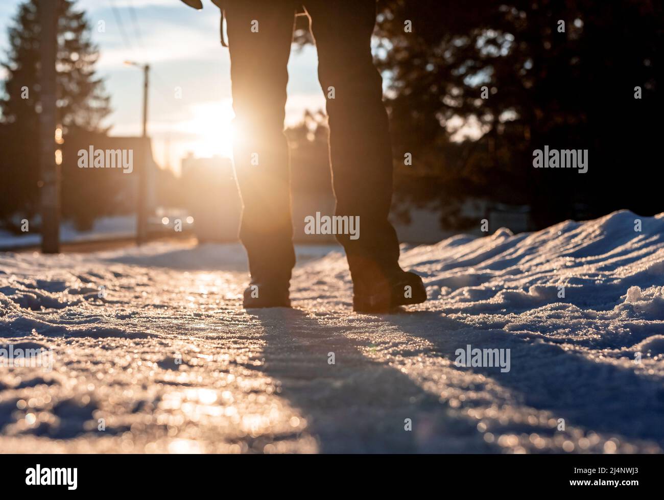 Uomo che cammina lungo la strada innevata. Piedi primo piano. Foto dal retro al sole. Foto di alta qualità Foto Stock