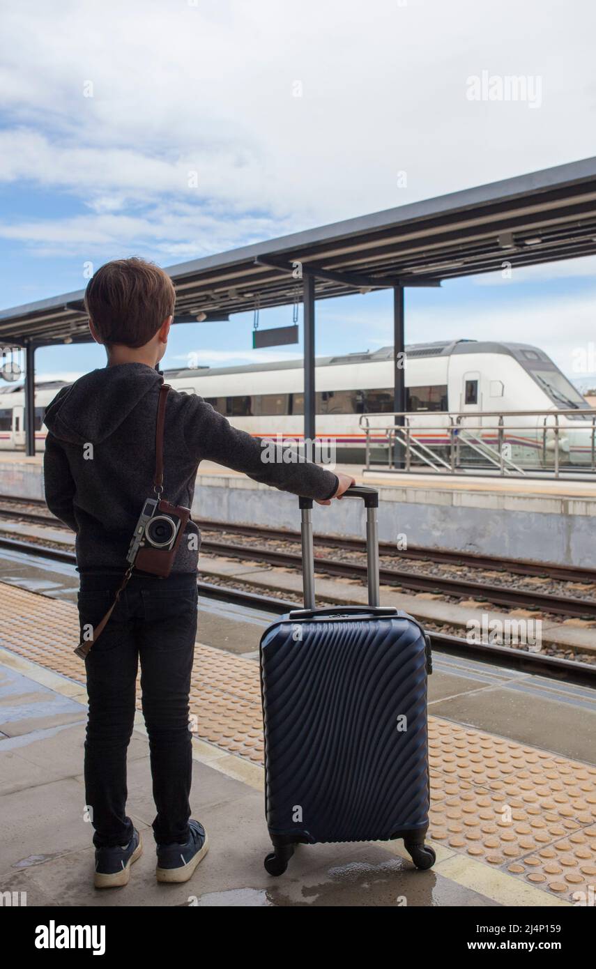 Bambino ragazzo alla stazione ferroviaria con carrello. Viaggio in treno con bambini concetto Foto Stock