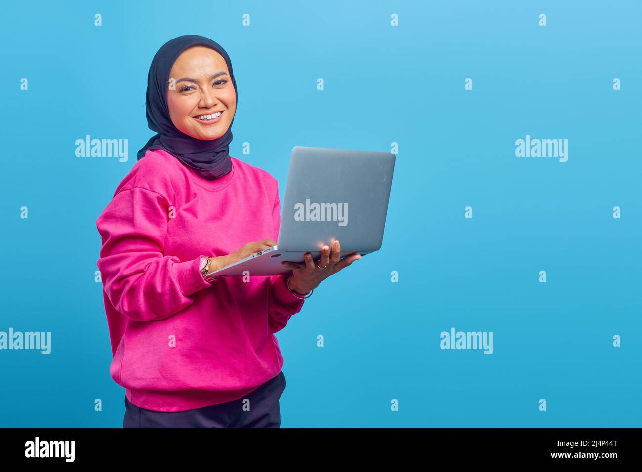 Primo piano della ragazza musulmana asiatica, tenendo il portatile in mano su sfondo blu Foto Stock