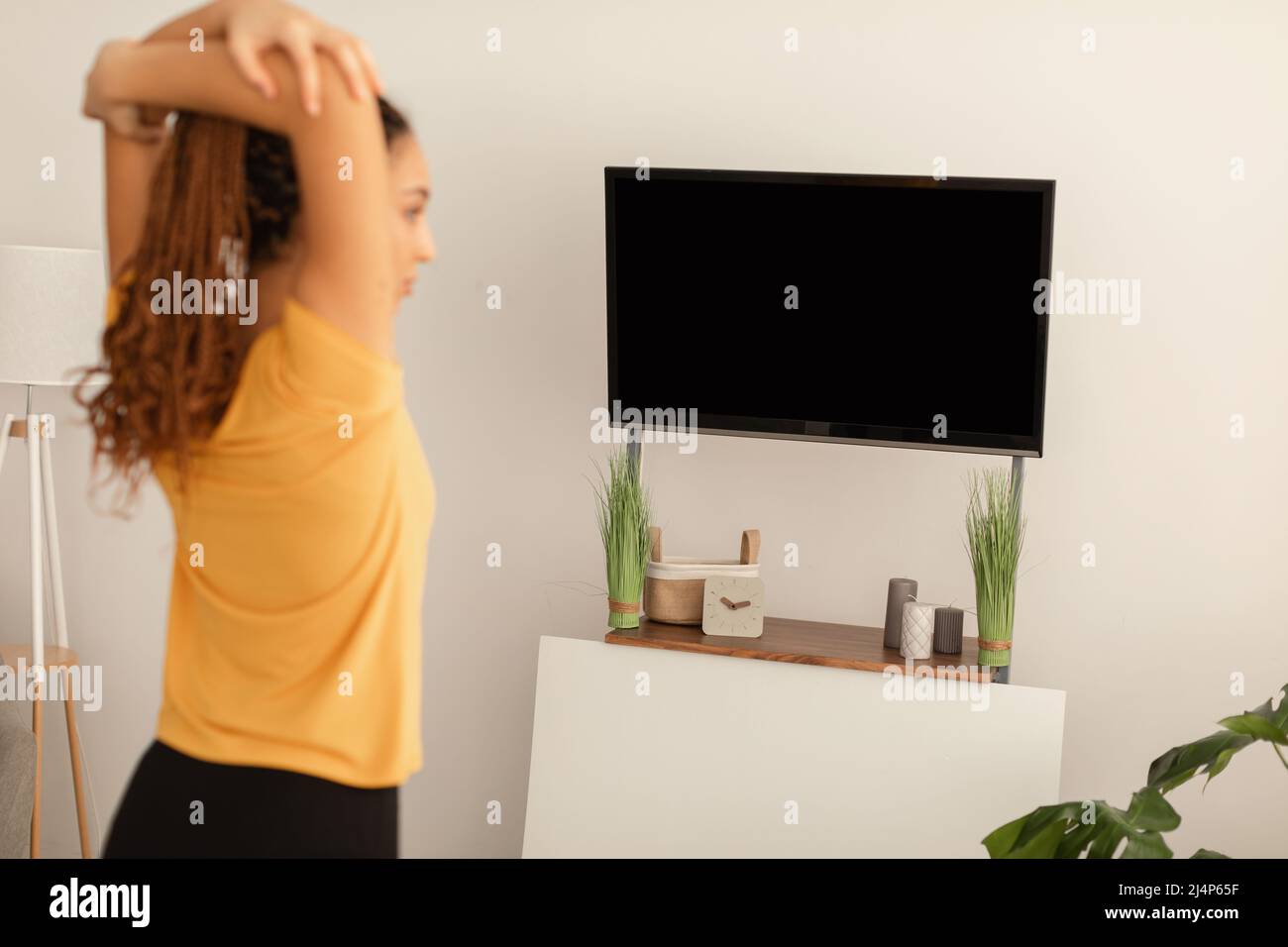 Black Woman Stretching Arms esercitandosi guardando schermo della televisione all'interno Foto Stock