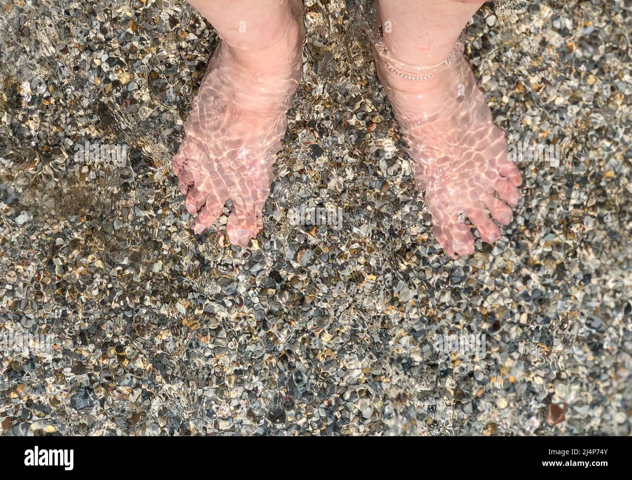mare, vista dall'alto bellissimi piedi di una donna bianca caucasica in piedi nel mare con piccole pietre di ciottoli o rocce. estate vacanza sfondo foto concetto Foto Stock