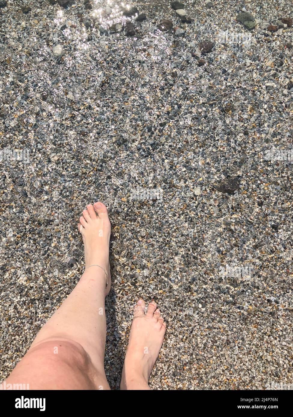 mare, vista dall'alto bellissimi piedi di una donna bianca caucasica che cammina in mare con piccole pietre di ciottoli o rocce. estate vacanza sfondo concetto foto o Foto Stock