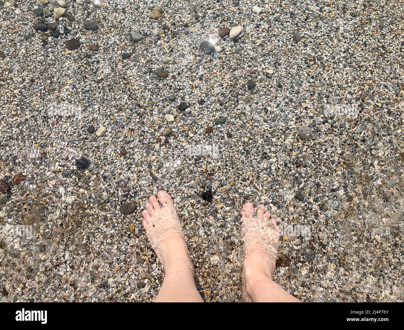 piede, vista dall'alto bellissimi piedi di una donna bianca caucasica in piedi in mare con piccole pietre di ciottoli o rocce. estate vacanza sfondo foto concetto Foto Stock