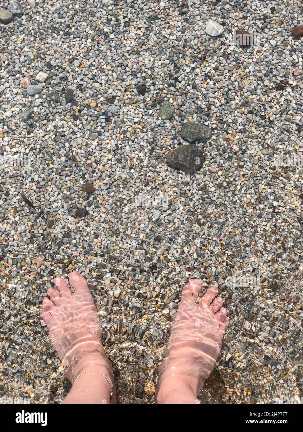 mare, vista dall'alto bellissimi piedi di una donna bianca caucasica in piedi nel mare con piccole pietre di ciottoli o rocce. estate vacanza sfondo foto concetto Foto Stock