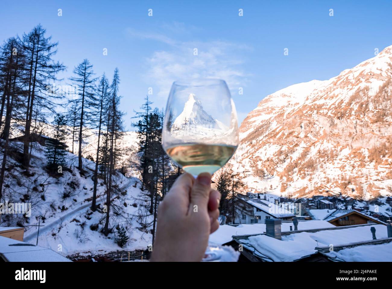 Uomo in possesso di wineglass visione Cervino e paesaggio di città coperto di neve contro il cielo Foto Stock