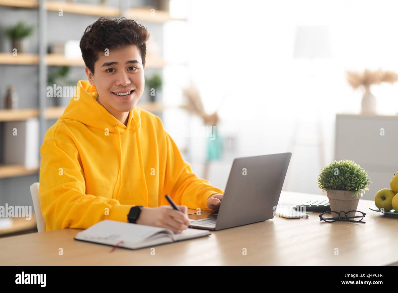 Uomo asiatico sorridente che lavora su un computer portatile e scrive Foto Stock