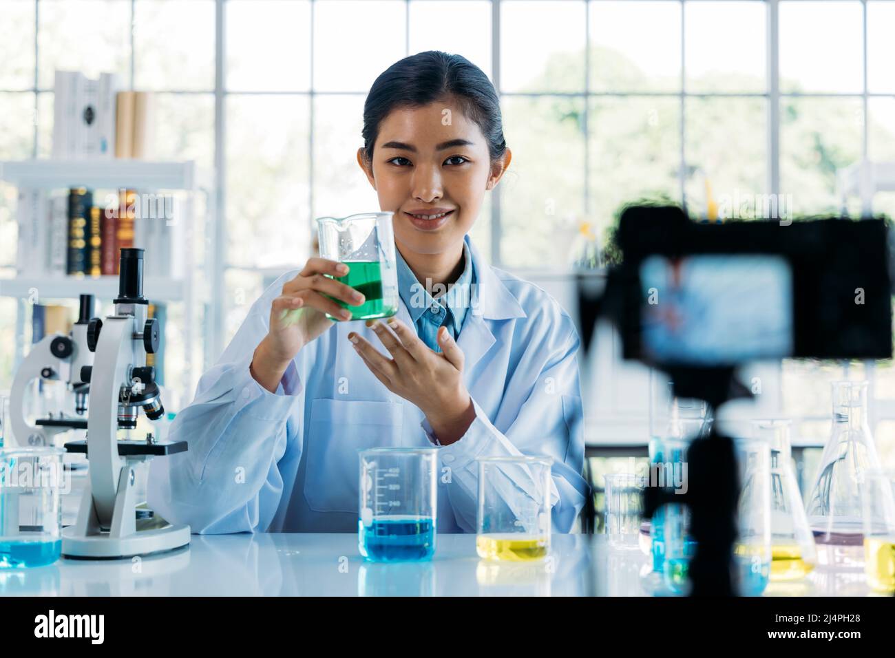 Ritratto di giovane dottore che indossa camice da laboratorio registrazione online video class e vlog sulla ricerca medica e gli esperimenti scientifici in laboratorio Foto Stock