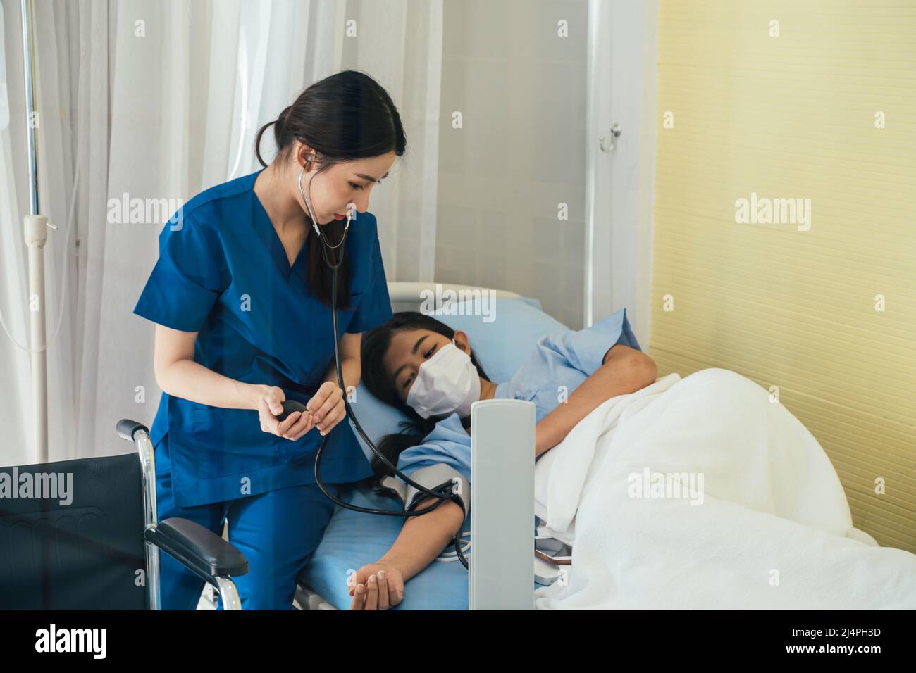 Giovane medico in seduta uniforme oltre a debole paziente femminile con maschera di controllo della pressione sanguigna con macchina e stetoscopio in ospedale Foto Stock