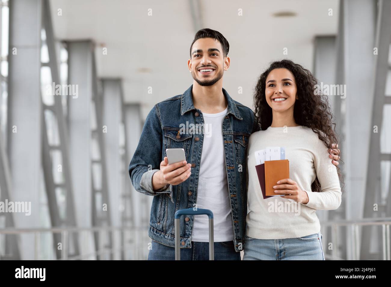 Sposi arabi pronti per il viaggio, in attesa in aeroporto con passaporti e smartphone Foto Stock