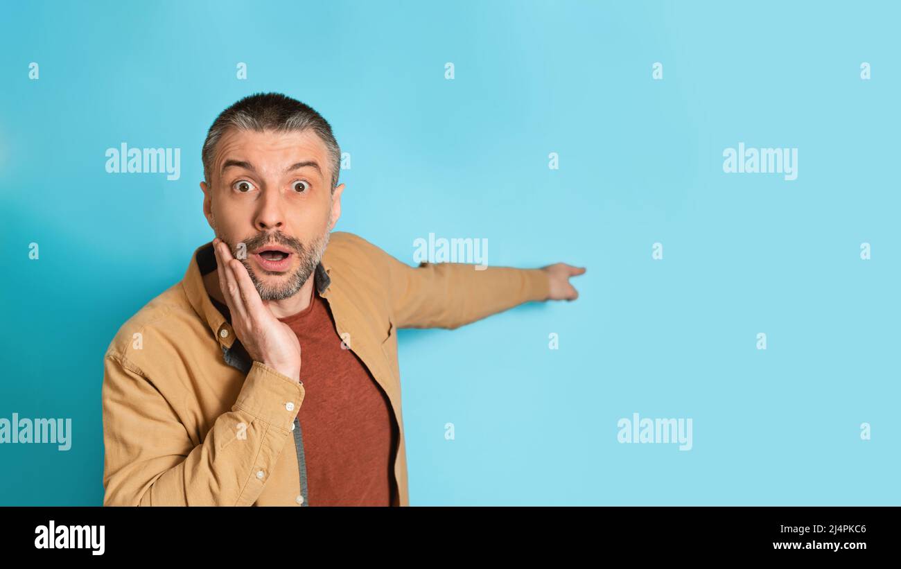 Shocked Man puntando dito da parte a spazio vuoto, sfondo blu Foto Stock