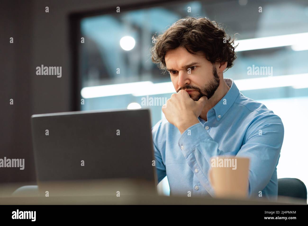 Uomo d'affari concentrato che utilizza un computer portatile seduto alla scrivania Foto Stock