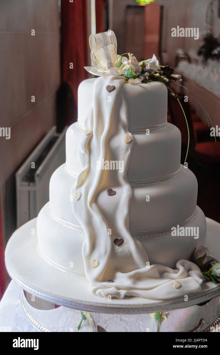 Nastro e fiori sulla parte superiore di una torta di nozze ghiacciata bianca. Foto Stock