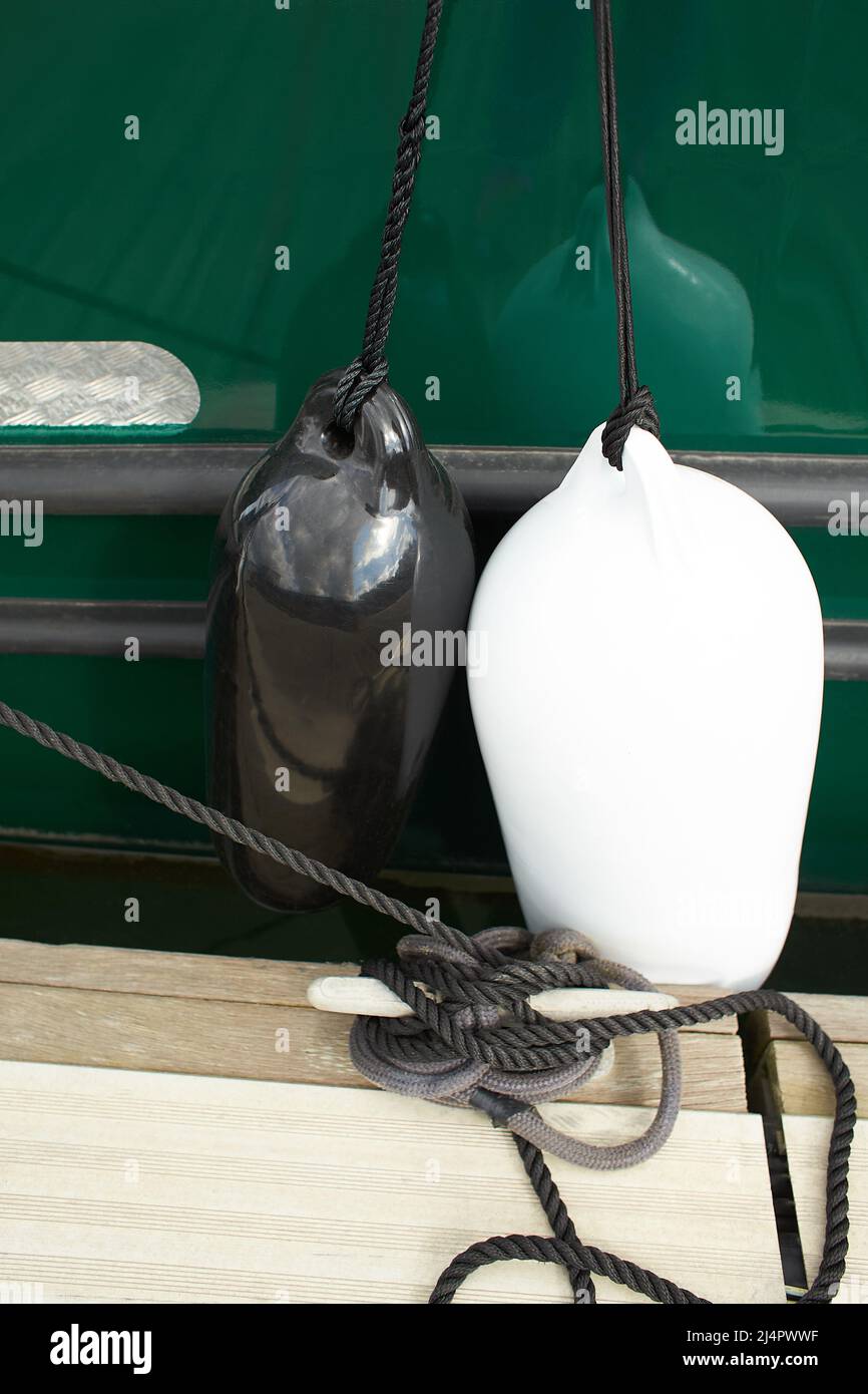 Parafanghi bianchi e neri sospesi tra una barca e il molo per la protezione. Parafanghi marittimi Foto Stock