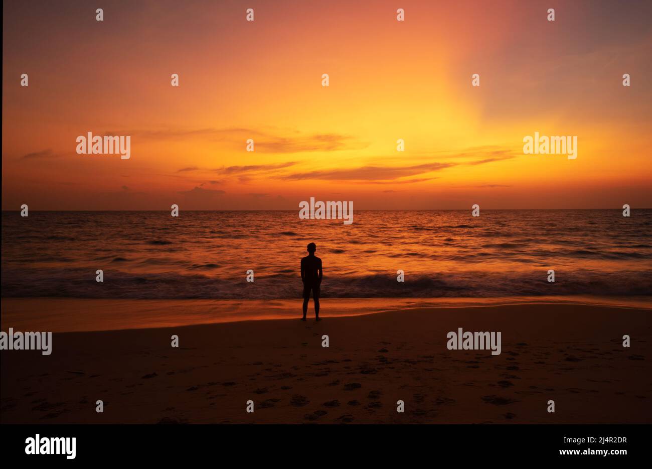 Un uomo in piedi sulla spiaggia di Naithon, Phuket e guardando il bellissimo cielo al tramonto. Foto Stock