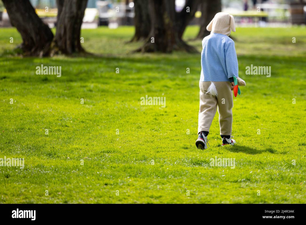 Erfurt, Germania. 17th Apr 2022. Un bambino in un costume di coniglio pasquale corre attraverso un prato in Ega Park. La domenica di Pasqua tutti i bambini fino ai 16 anni sono ammessi gratuitamente nel parco. Credit: Michael Reichel/dpa/Alamy Live News Foto Stock