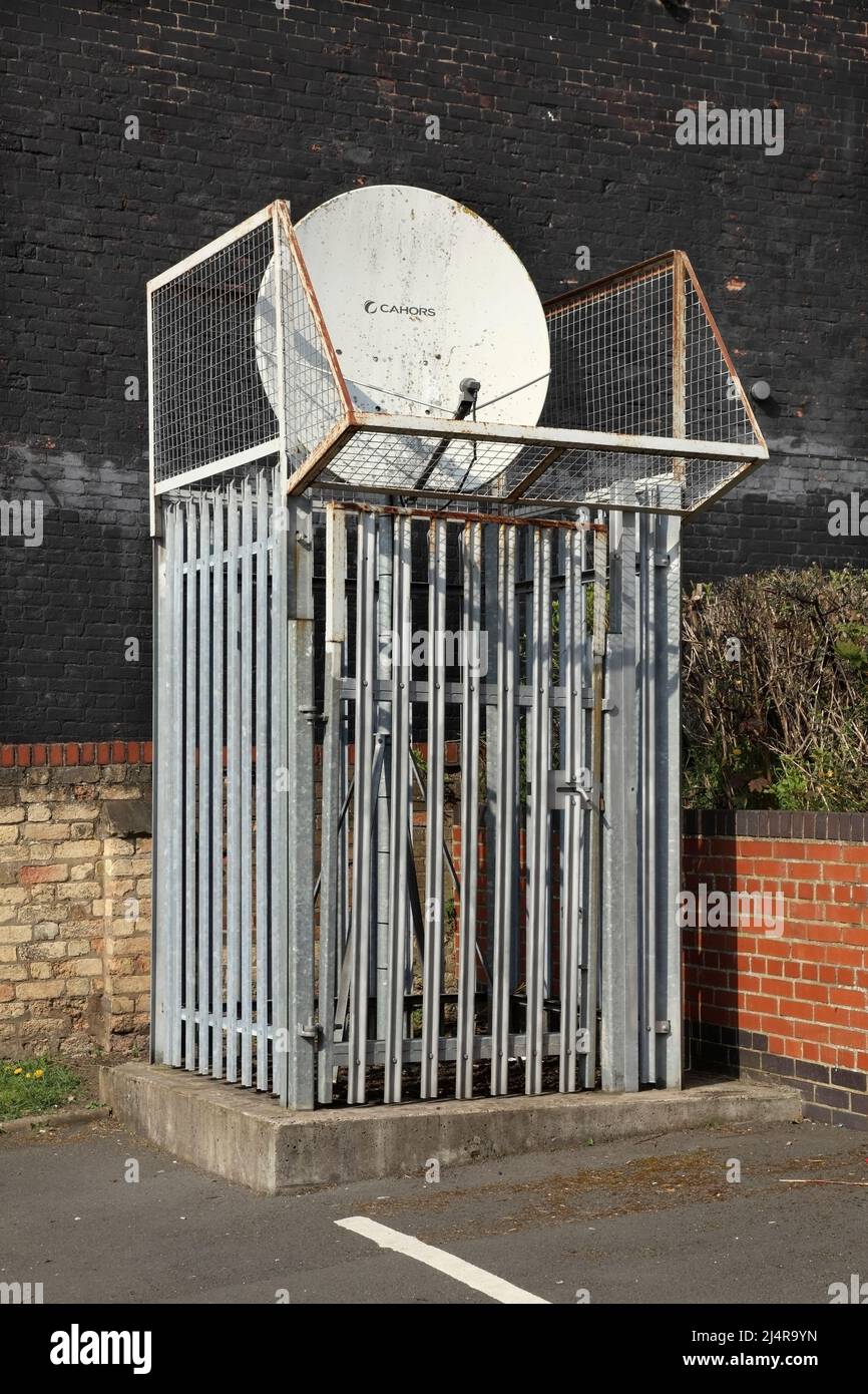 Antenna satellitare circondata da recinzioni in metallo ad alta sicurezza e rete antivandalismo. Foto Stock