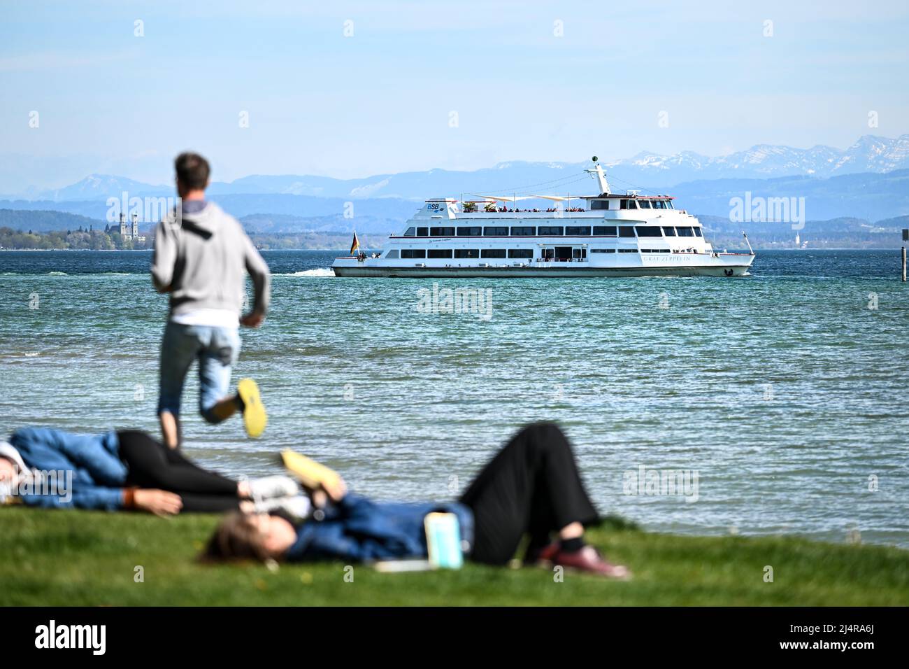 Immenstaad am Bodensee, Germania. 17th Apr 2022. La nave passeggeri Graf Zeppelin è ormeggiata di fronte a Immenstaad, mentre in primo piano gli escursionisti si trovano sul prato. Credit: Felix Kästle/dpa/Alamy Live News Foto Stock