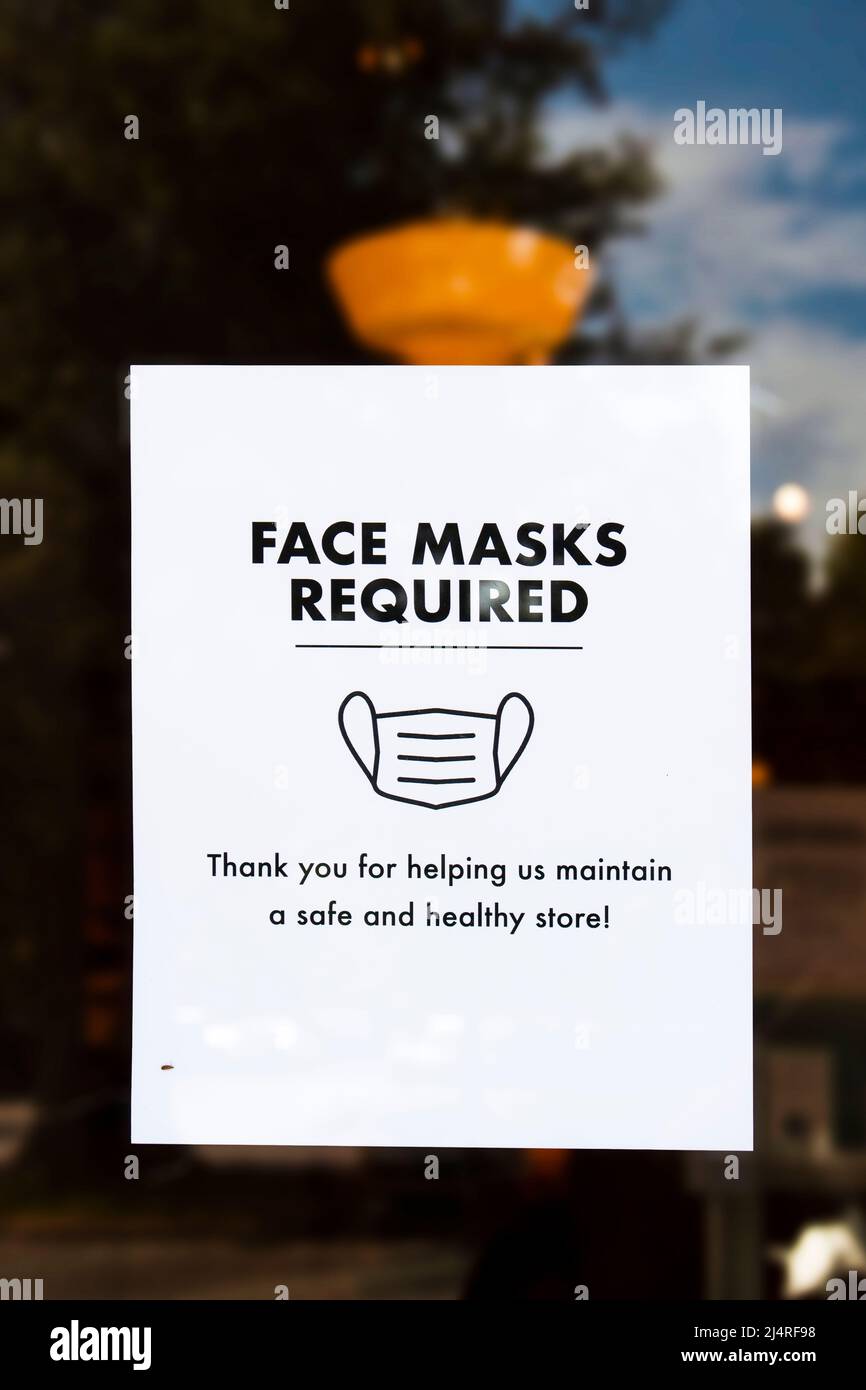 Maschera facciale richiesto segno sulla porta del negozio con riflesso di cielo e alberi intorno ad esso e bug strisciando su di esso Foto Stock