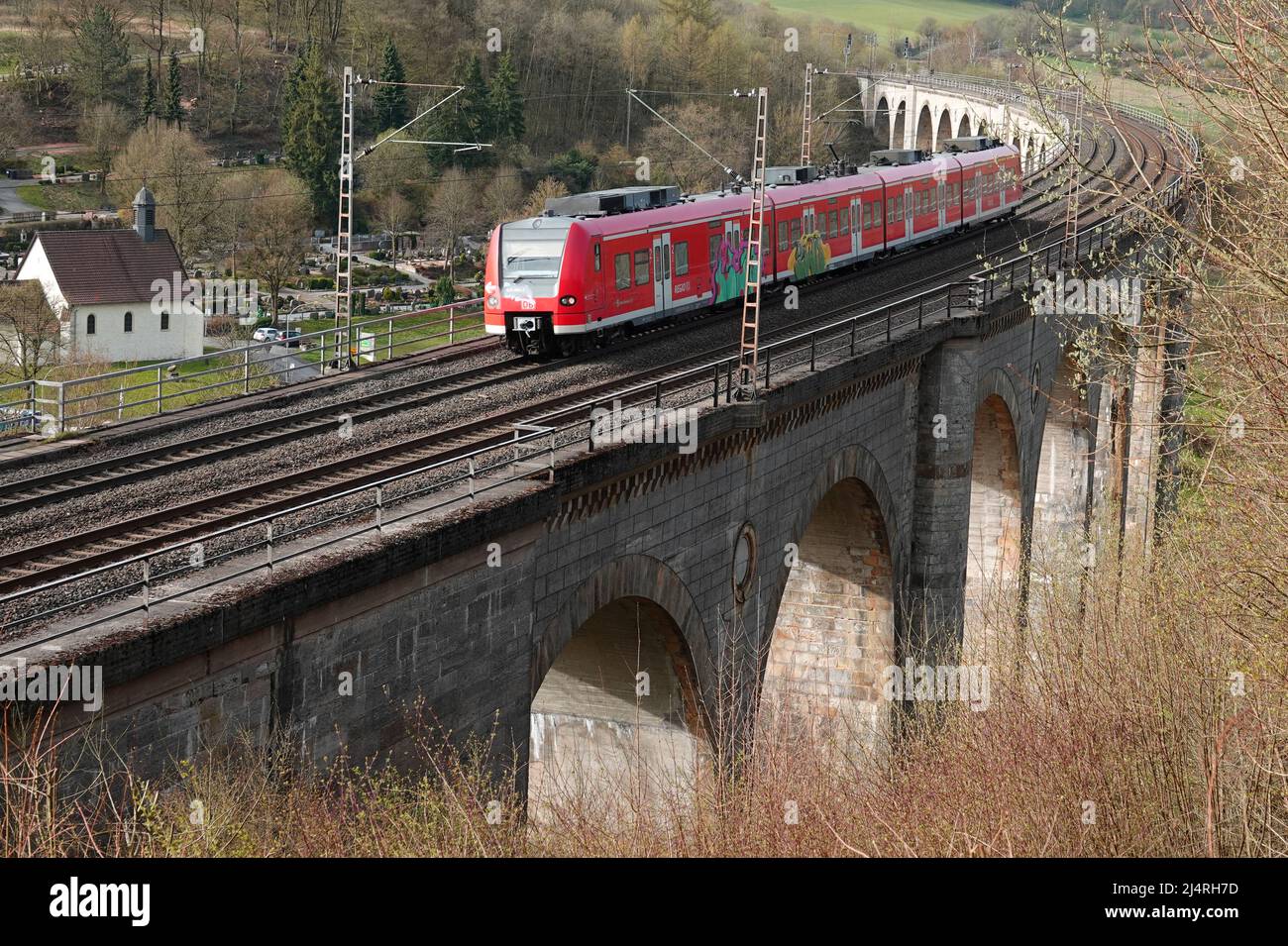 Altenbeken, Germania - Apr 13 2020 - Un treno rosso proveniente dalla compagnia ferroviaria tedesca DB Regio sta accelerando un vecchio viadotto ferroviario. Foto Stock