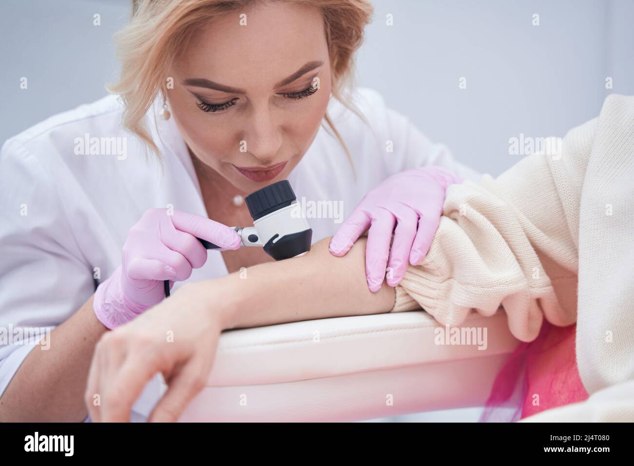 Medico attento che controlla la pelle del paziente con dermatoscopio Foto Stock