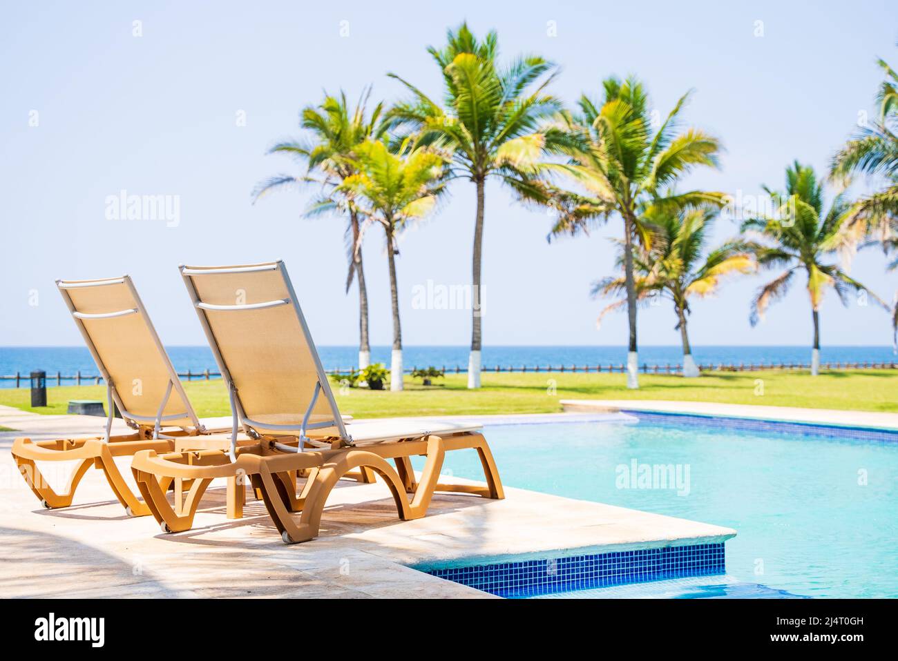 Letti a bordo piscina accanto alla piscina con vista sulle palme da cocco e sull'oceano Foto Stock