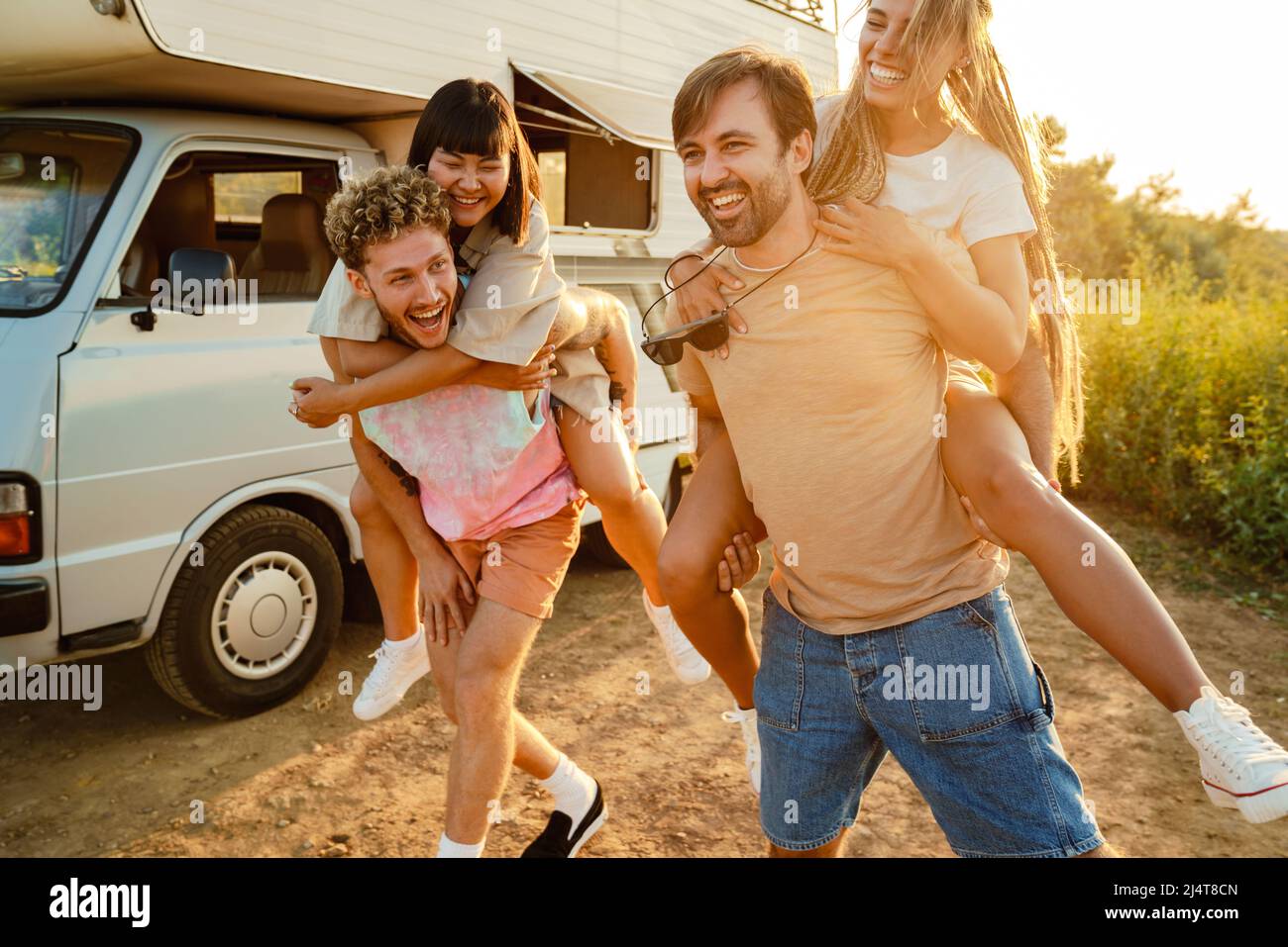 Multirazziale due coppie ridere e piggybacking da rimorchio all'aperto Foto Stock