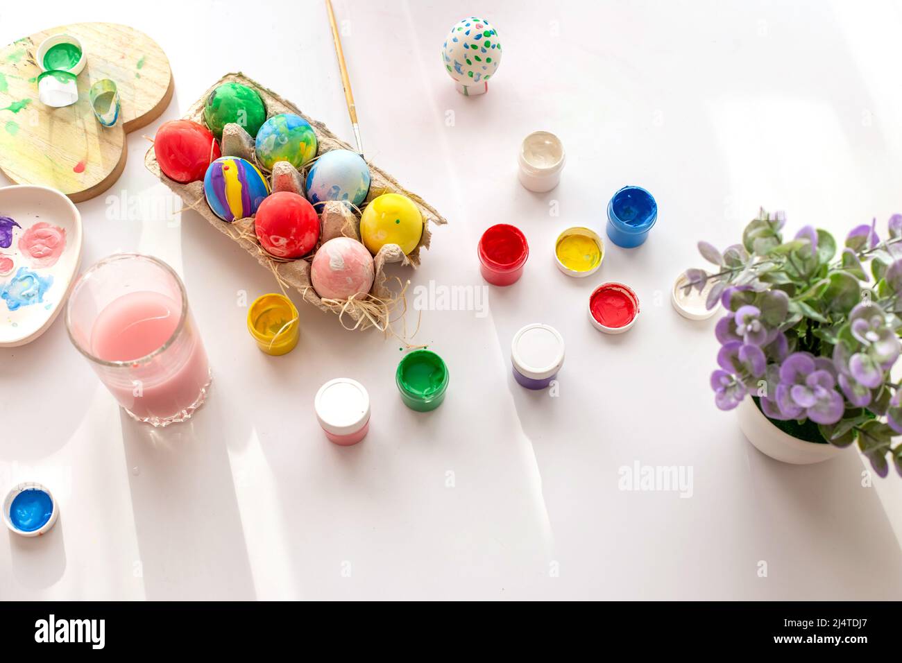 Su un tavolo bianco, alla luce del giorno, ci sono pennelli in un bicchiere d'acqua, uova multicolore in un vassoio, vasetti di vernice. Foto Stock
