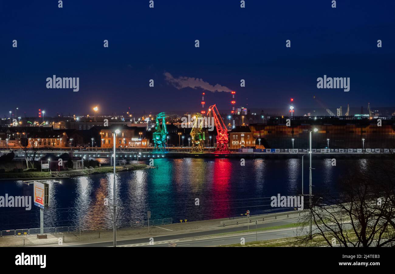 I tre vecchi porti si gru dall'isola di Szczecin di Lasztownia colorfully illuminato. Città di notte. Polonia. Dalla distanza che assomiglia ai dinosauri. P Foto Stock