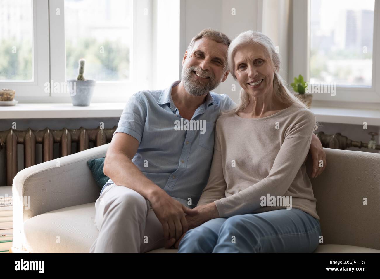 Felice amorevole coppia matura posa seduta sul divano a casa Foto Stock