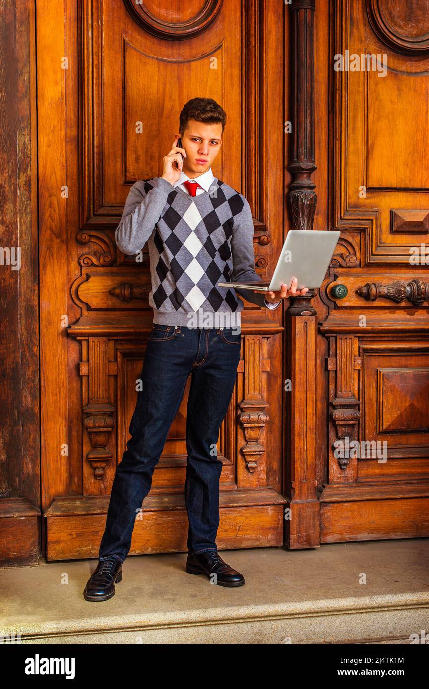 American College studente studiare, lavorare a New York. Indossando un  pullover a motivi geometrici, cravatta rossa, jeans blu, scarpe in pelle,  un ragazzo giovane si sta levando in piedi Foto stock -