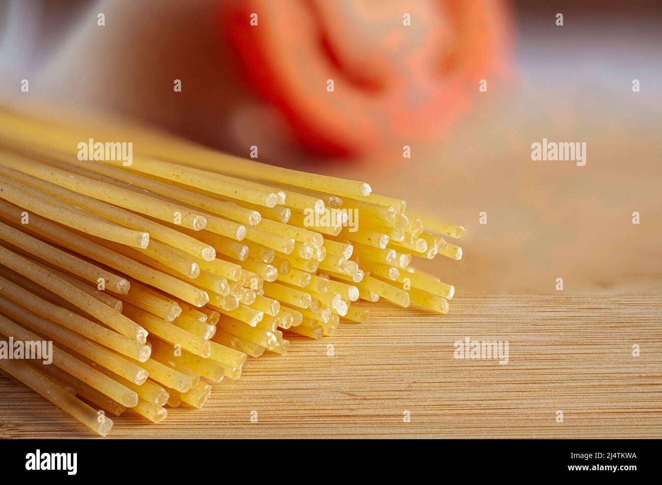 Pasta cruda o non cotta con un pomodoro rosso sfocato sullo sfondo e su un tagliere, vista laterale in orizzontale. Foto Stock