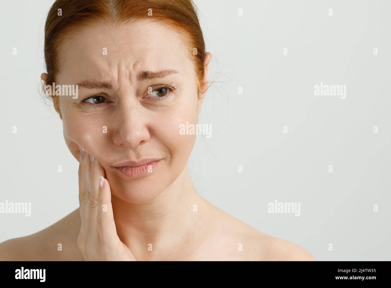 Una donna che soffre di forte dolore ai denti, toccando la guancia con la mano. Odontoiatria concetto. Foto Stock