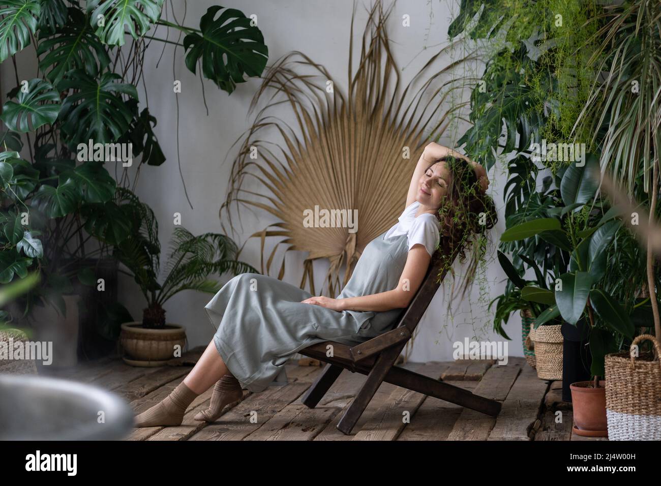 Donna sognante che si rilassa nel giardino tropicale in stile resort a casa, donna giardiniere riposante in serra Foto Stock
