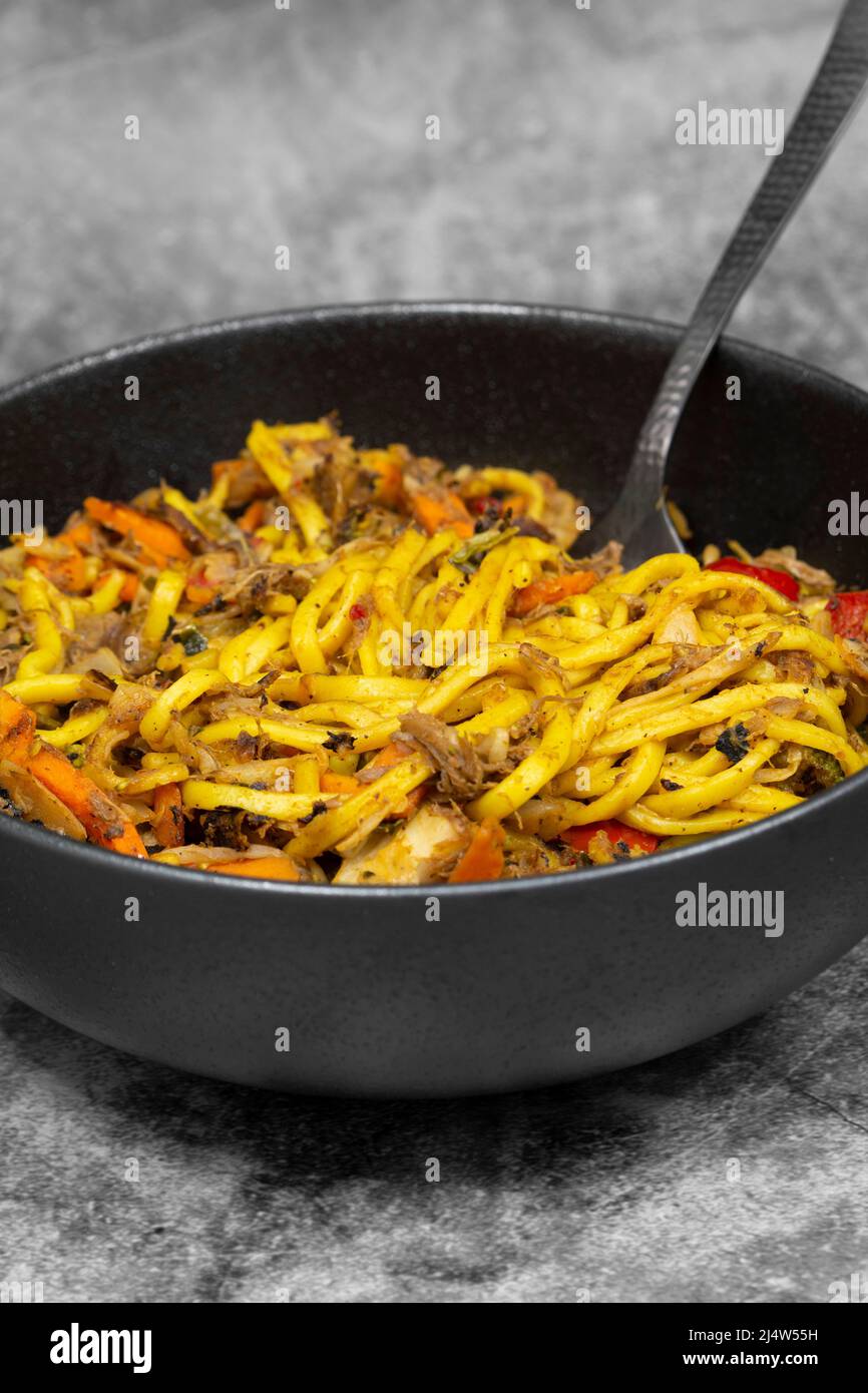 Anatra grattugiata mescolare friggere con spezie e verdure in un recipiente nero. Su sfondo di pietra Foto Stock