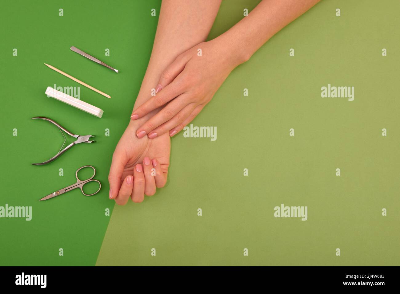 Mani con manicure di colore naturale accanto agli strumenti per la procedura su sfondo verde Foto Stock