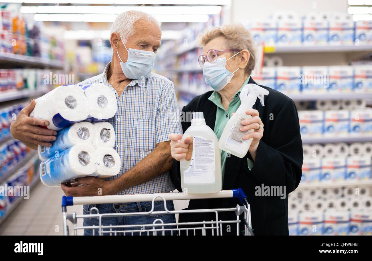 coppia matura indossando maschera e guanti con protezione covid sceglie asciugamani di carta nel reparto di supermercato Foto Stock