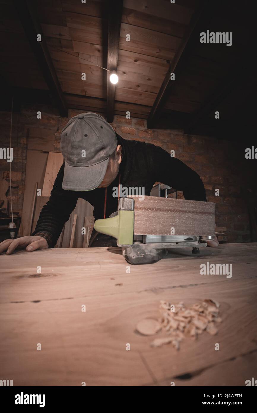 Un falegname lavora in un'officina. Smerigliatrici per falegnami, produzione di mobili. Un falegname sta macinando una parte di legno con una levigatrice elettrica. Foto Stock