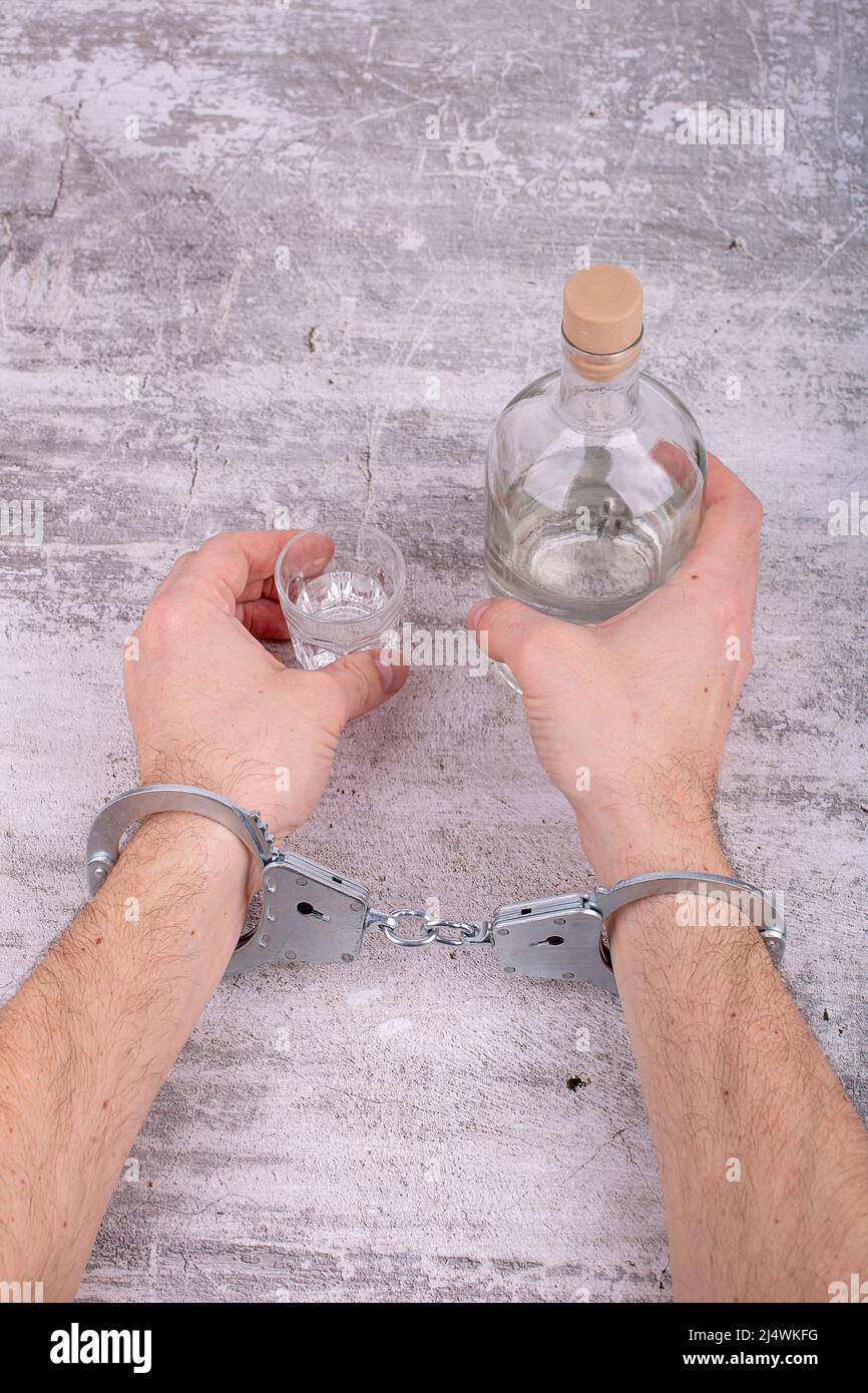 Il concetto di dipendenza da alcol maschile. Le mani di uomini con un polsone di mano tengono una bottiglia e un bicchiere di alcol. Foto Stock