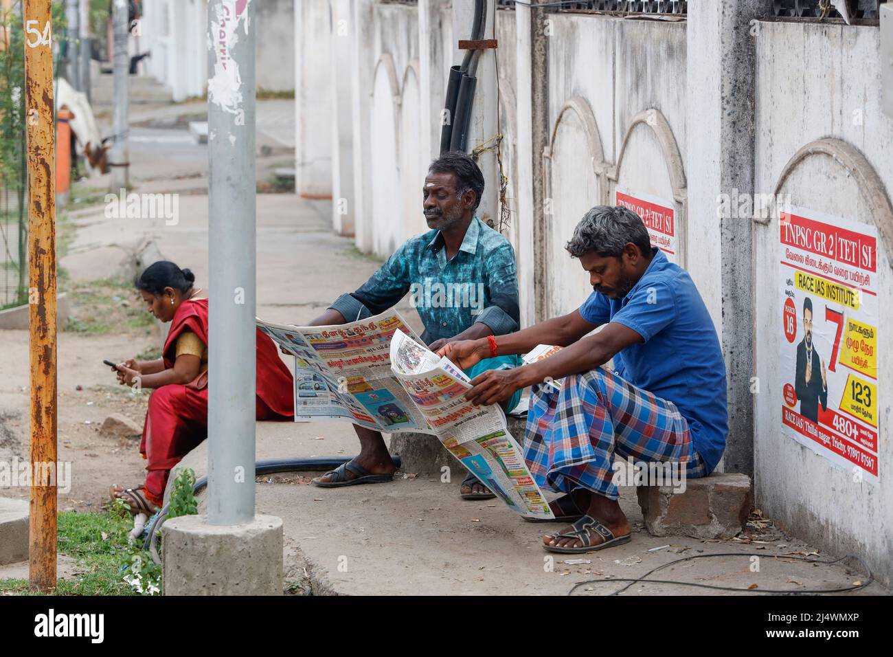 Due uomini che leggono il giornale su un marciapiede a Trichy, Tamil Nadu, India Foto Stock