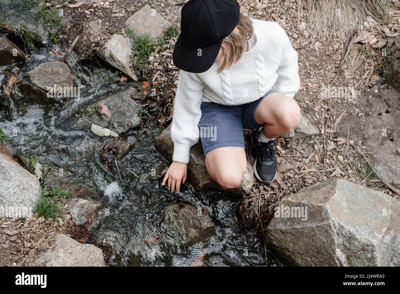 Giovane ragazza seduta da un torrente che tocca l'acqua Foto Stock