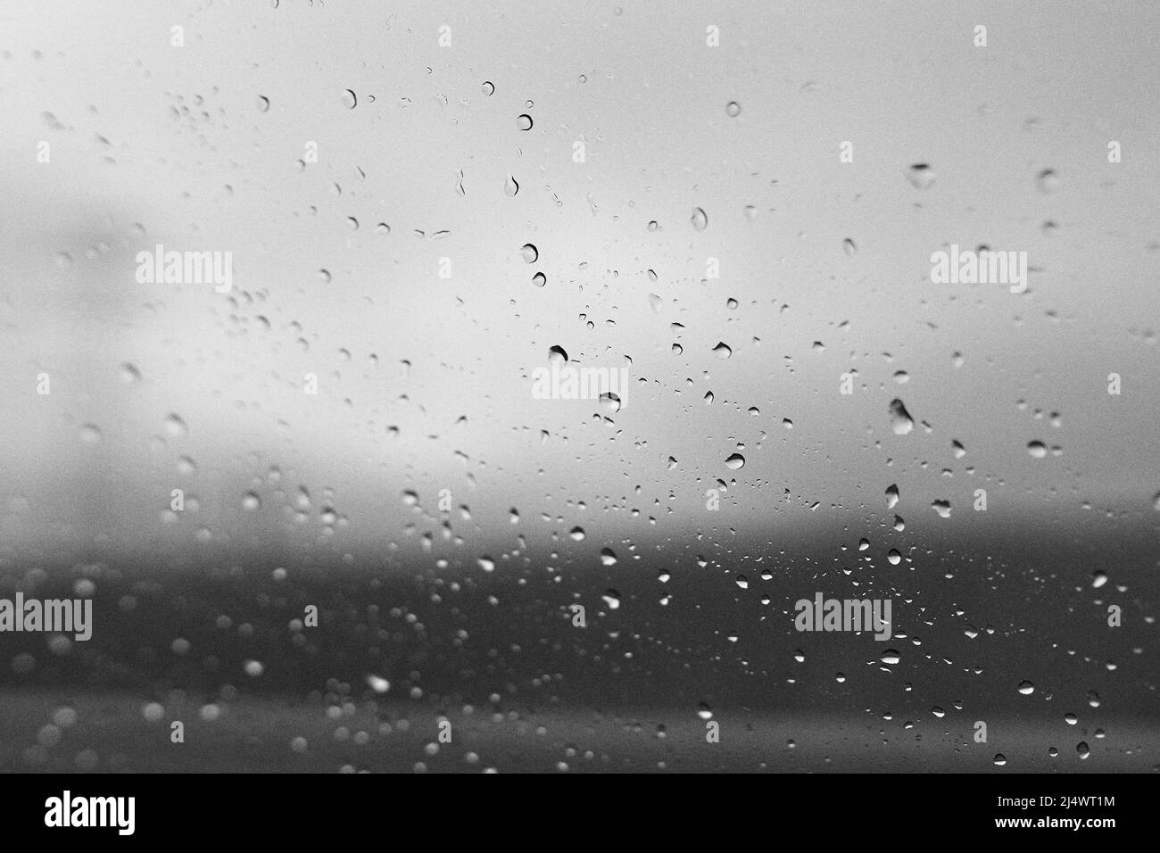 Gocce di pioggia sul vetro della finestra con sfondo sfocato in bianco e nero Foto Stock